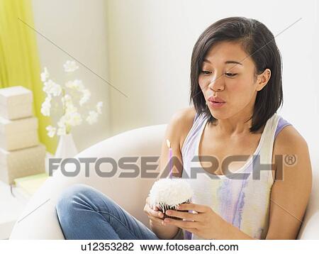 Young woman holding cupcake and blowing out candle View Large Photo Image Stock Image - Young woman holding cupcake and blowing out candle. Fotosearch
