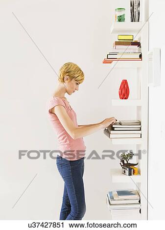 Stock Image - Young woman standing near bookshelf. Fotosearch