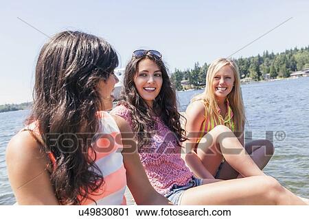 Stock Image - Young women hanging out by lake. Fotosearch