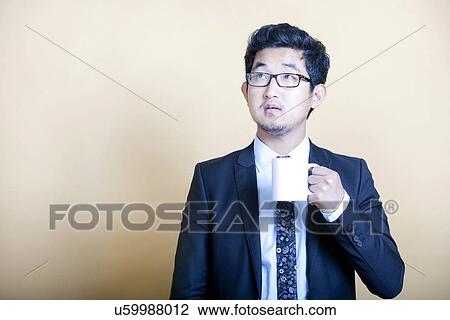 Stock Image - Asian businessman drinking cup of coffee. Fotosearch