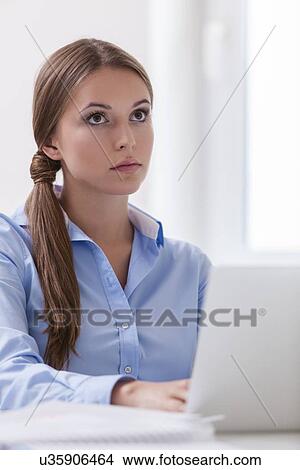 Beautiful businesswoman sitting on desk and looking at laptop View Large Photo Image Picture - Beautiful businesswoman sitting on desk and looking at laptop . Fotosearch
