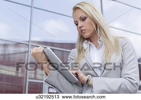 Stock Image - Beautiful businesswoman using digital tablet against office building. Fotosearch