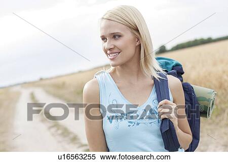 Stock Photography - Beautiful female hiker with backpack looking away while standing on field. Fotosearch