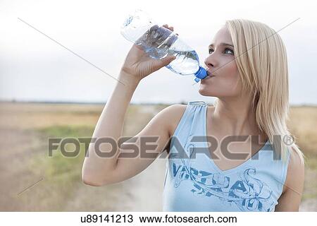 Beautiful woman drinking water from bottle while standing on field View Large Photo Image Stock Image - Beautiful woman drinking water from bottle while standing on field. Fotosearch