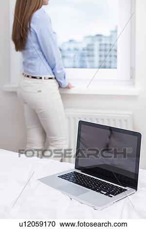 Stock Image - Beautiful woman staring out of window with laptop in foreground. Fotosearch