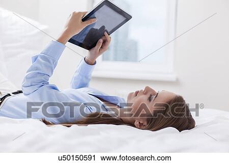 Stock Image - Beautiful woman using tablet computer on her bed. Fotosearch