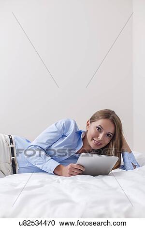 Stock Image - Beautiful woman using tablet computer on her bed. Fotosearch