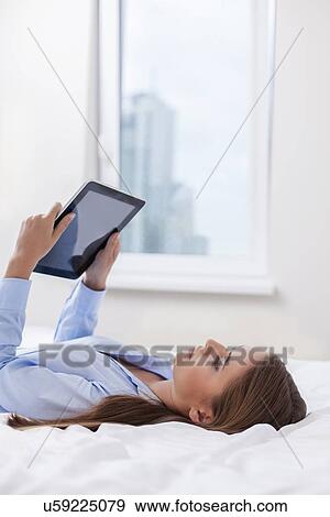 Stock Photo - Beautiful woman using tablet computer on her bed. Fotosearch