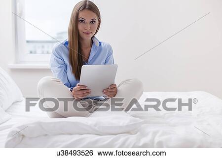 Stock Photograph - Beautiful woman using tablet computer on her bed. Fotosearch