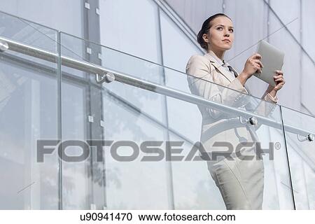 Beautiful young businesswoman holding tablet computer at office railing View Large Photo Image Stock Image - Beautiful young businesswoman holding tablet computer at office railing. Fotosearch