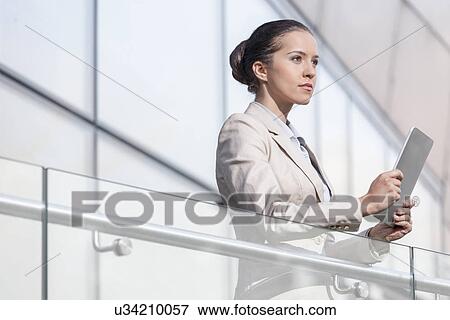 Beautiful young businesswoman holding digital tablet at office railing View Large Photo Image Stock Photo - Beautiful young businesswoman holding digital tablet at office railing. Fotosearch