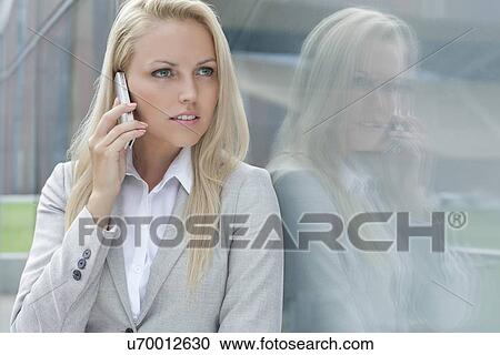 Beautiful young businesswoman conversing on cell phone while looking away by glass wall View Large Photo Image Stock Image - Beautiful young businesswoman conversing on cell phone while looking away by glass wall. Fotosearch