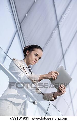 Stock Image - Beautiful young businesswoman using tablet computer at office railing. Fotosearch
