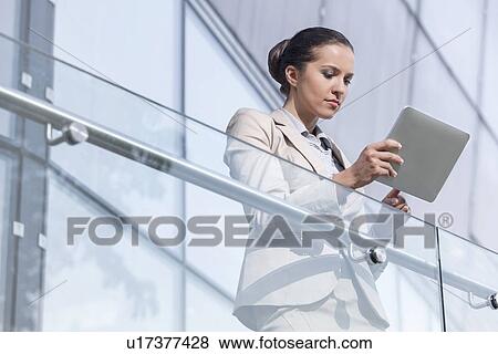Stock Photo - Beautiful young businesswoman using digital tablet at office railing. Fotosearch