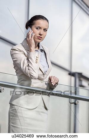 Stock Photo - Beautiful young businesswoman using smart phone at office railing. Fotosearch