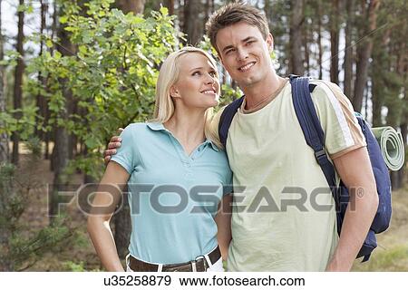 Stock Photo - Beautiful young woman looking at man while hiking in forest. Fotosearch