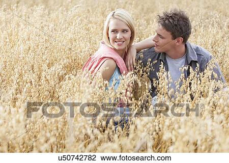 Beautiful young woman looking away while sitting with boyfriend amidst field View Large Photo Image Stock Image - Beautiful young woman looking away while sitting with boyfriend amidst field. Fotosearch