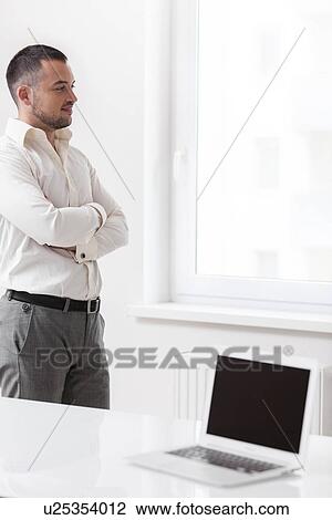 Businessman staring out of window with laptop in foreground View Large Photo Image Stock Image - Businessman staring out of window with laptop in foreground. Fotosearch