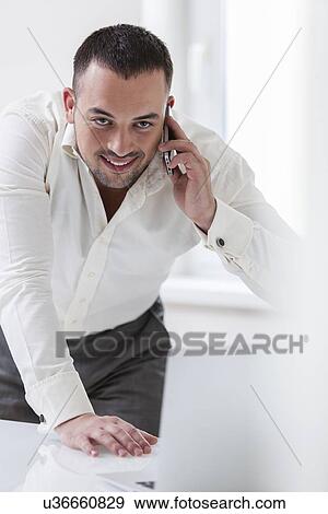 Businessman using mobile phone and looking at computer View Large Photo Image Stock Photo - Businessman using mobile phone and looking at computer. Fotosearch