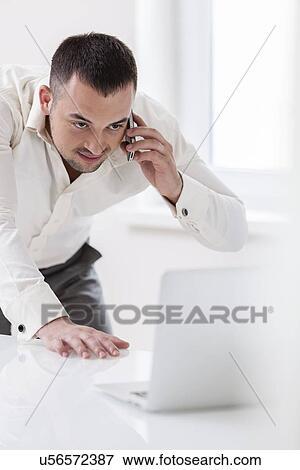 Businessman using mobile phone and looking at computer View Large Photo Image Stock Photo - Businessman using mobile phone and looking at computer. Fotosearch