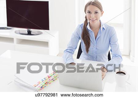 Stock Image - Businesswoman looking bored in front of laptop and television. Fotosearch