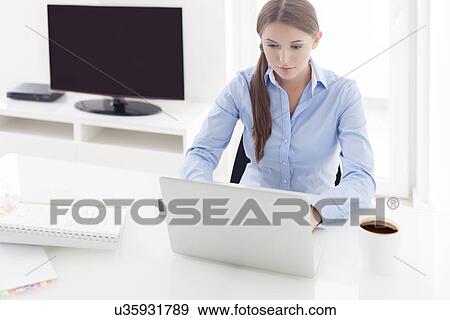 Stock Photo - Businesswoman working on her laptop in front of television. Fotosearch