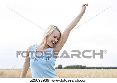 Cheerful young woman with arm raised standing against clear sky View Large Photo Image Stock Photo - Cheerful young woman with arm raised standing against clear sky. Fotosearch