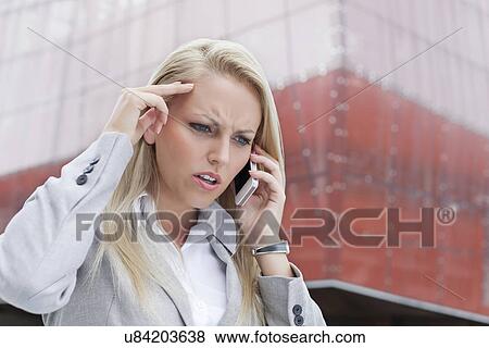 Close-up of angry businesswoman conversing on cell phone against office building View Large Photo Image Stock Photo - Close-up of angry businesswoman conversing on cell phone against office building. Fotosearch