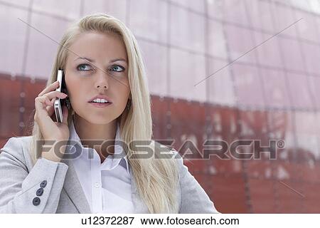 Close-up of young businesswoman communicating on mobile phone against office building View Large Photo Image Stock Photo - Close-up of young businesswoman communicating on mobile phone against office building. Fotosearch