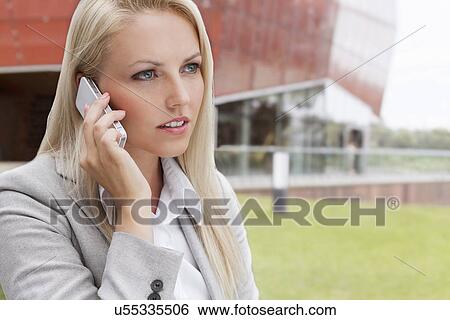 Close-up of young businesswoman conversing on mobile phone against office building View Large Photo Image Stock Photograph - Close-up of young businesswoman conversing on mobile phone against office building. Fotosearch