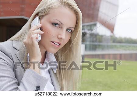 Close-up portrait of beautiful young businesswoman communicating on mobile phone against office building View Large Photo Image Stock Image - Close-up portrait of beautiful young businesswoman communicating on mobile phone against office building. Fotosearch