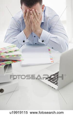 Stock Photography - Close-up view of Caucasian businessman with heads in hands at his desk. Fotosearch
