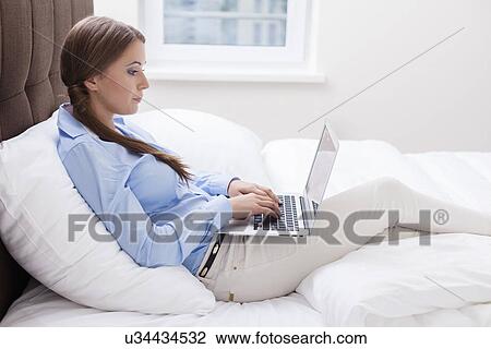 Close-up view of Woman using laptop on her bed View Large Photo Image Stock Image - Close-up view of Woman using laptop on her bed. Fotosearch