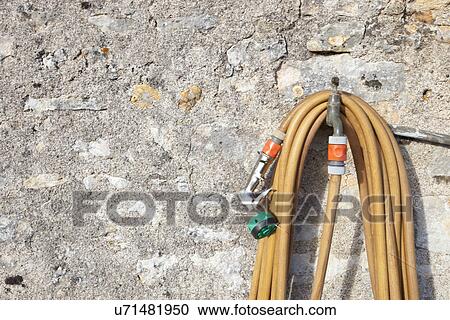 Coiled garden hose hanging on faucet against stone wall View Large Photo Image Stock Image - Coiled garden hose hanging on faucet against stone wall. Fotosearch