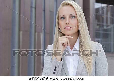 Confident businesswoman with hand on chin looking away against office building View Large Photo Image Stock Photo - Confident businesswoman with hand on chin looking away against office building. Fotosearch