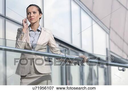 Confident young businesswoman using cell phone at office balcony View Large Photo Image Stock Photo - Confident young businesswoman using cell phone at office balcony. Fotosearch