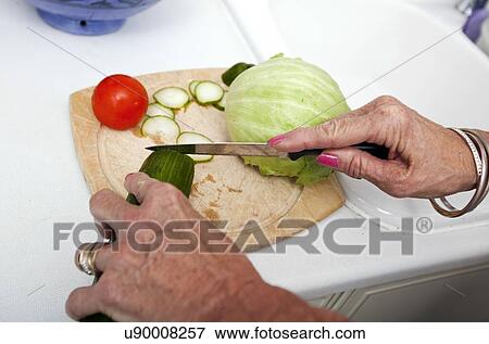 Stock Photo - Cropped image of senior woman chopping vegetables on cutting board in kitchen. Fotosearch