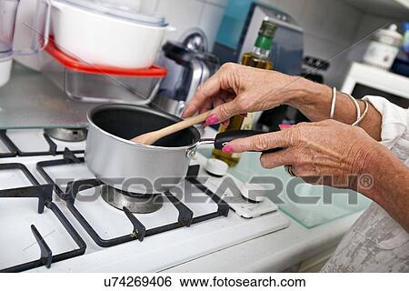 Stock Photograph - Cropped image of senior woman cooking at kitchen counter. Fotosearch