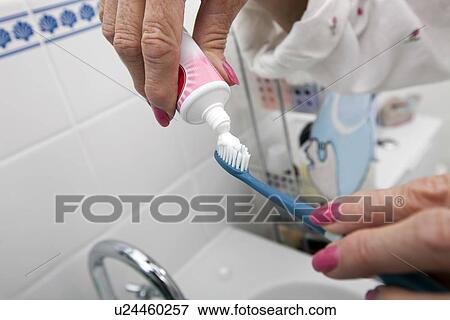 Stock Photo - Cropped image of senior woman putting tooth paste on brush at home. Fotosearch