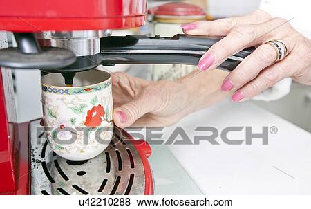 Stock Photo - Cropped image of woman dispensing coffee from machine in kitchen. Fotosearch
