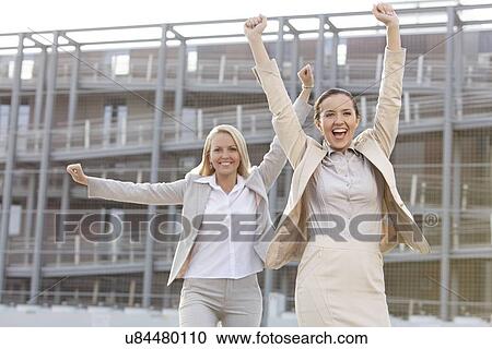 Excited young businesswomen with arms raised against office building View Large Photo Image Stock Image - Excited young businesswomen with arms raised against office building. Fotosearch