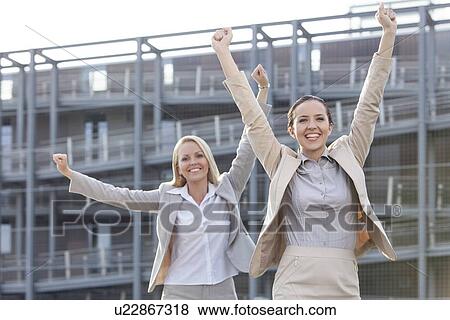 Excited young businesswomen with arms raised against office building View Large Photo Image Stock Photo - Excited young businesswomen with arms raised against office building. Fotosearch