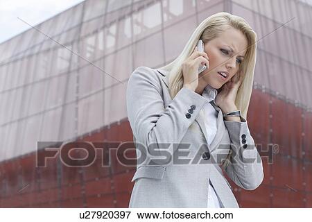 Stock Photo - Frustrated businesswoman in suit conversing on cell phone against office building. Fotosearch