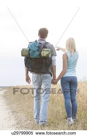 Stock Photography - Full length of female hiker showing something to man on field. Fotosearch