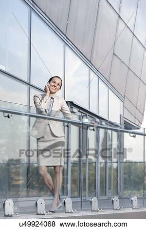 Full length of happy young businesswoman using cell phone at office balcony View Large Photo Image Stock Photo - Full length of happy young businesswoman using cell phone at office balcony. Fotosearch