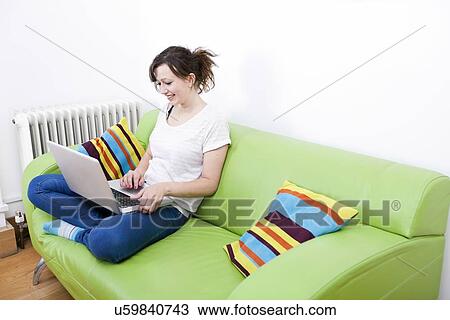 Full length of happy young woman using laptop while sitting on green sofa View Large Photo Image Stock Image - Full length of happy young woman using laptop while sitting on green sofa. Fotosearch