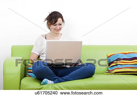 Full length of happy young woman using laptop while sitting on green sofa View Large Photo Image Stock Image - Full length of happy young woman using laptop while sitting on green sofa. Fotosearch
