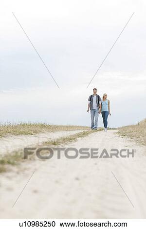 Stock Image - Full length of young hiking couple walking on path at field. Fotosearch