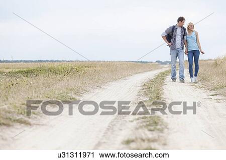Stock Image - Full length of young hiking couple standing on trail at field. Fotosearch