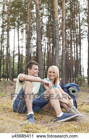 Stock Image - Full length of young hiking couple relaxing in forest. Fotosearch